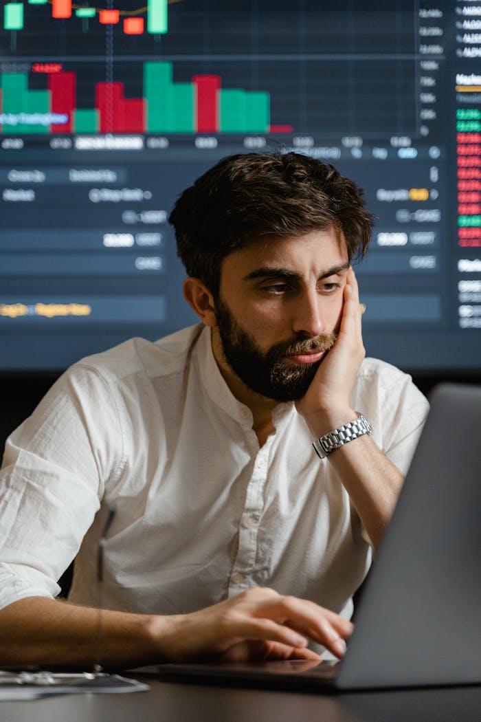 Businessman in office analyzing stock market data on a laptop with a financial chart in the background.